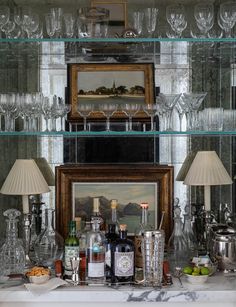 an assortment of wine glasses and liquor bottles on a shelf in front of a painting