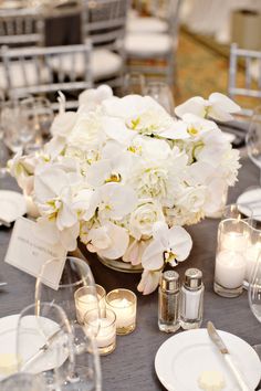 the centerpieces on this table are filled with white flowers, candles and place cards