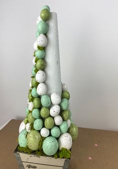 an artificial christmas tree made out of eggs and moss is displayed on a cardboard box