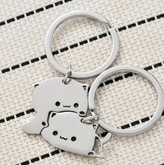 two metal key chains sitting on top of a white cloth covered floor with an animal shaped key chain attached to it