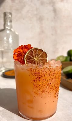 a drink with orange and sprinkles on the rim next to limes