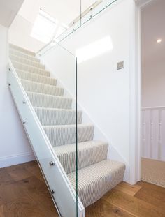 a stair case with glass railings and white carpet on the bottom, next to a wooden floor