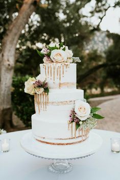 a three tiered cake with flowers and dripping icing on the top is sitting on a table