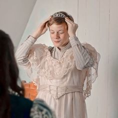 a woman wearing a tiara standing in front of a mirror with her hands on her head