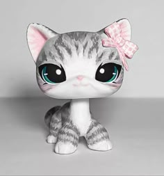 a small gray and white cat with a pink bow on it's head, sitting in front of a grey background