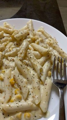 a white plate topped with macaroni and cheese covered in seasoning next to a fork