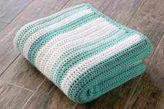 a green and white crocheted blanket laying on the floor next to a wooden floor