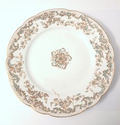 a white and gold plate with an ornate design on the rim, against a white background