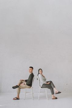 two people sitting on chairs in front of a white wall