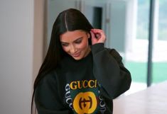 a woman wearing a gucci sweatshirt and holding a cell phone to her ear while walking down a hallway