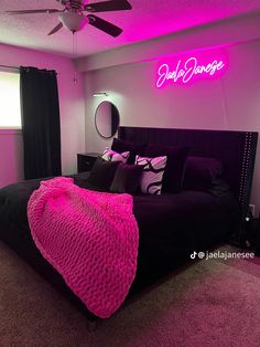 a bedroom with pink lighting and black bed in the center, along with a neon sign above it