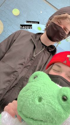 two people wearing masks and one is holding a green stuffed animal in front of them