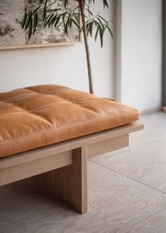 a brown leather bench sitting on top of a hard wood floor next to a potted plant