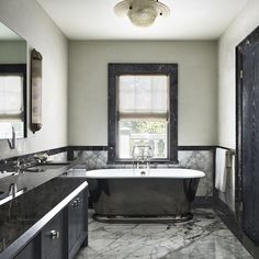 a large bathroom with marble floors and black bathtub in the center, along with two sinks