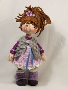 a crocheted doll with brown hair and purple dress is posed on a white background