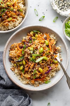 two bowls filled with rice and vegetables on top of a white table next to spoons