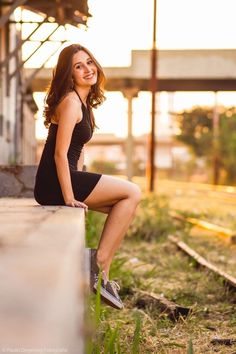 a beautiful young woman sitting on the side of a train track posing for a photo