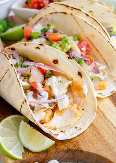 three fish tacos on a wooden cutting board with limes and cilantro