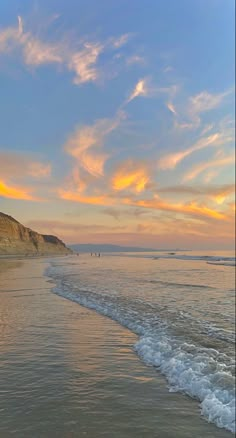 the sun is setting at the beach with people walking in the water and on the sand