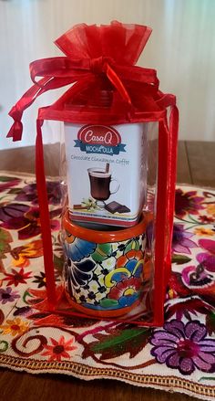 a candle with a red ribbon around it on top of a colorful table cloth next to a glass container