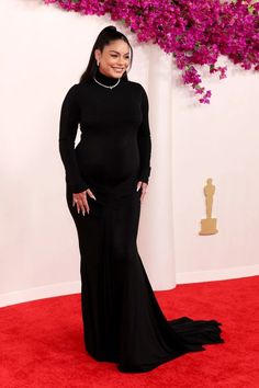 pregnant woman in black gown posing for the camera on red carpet with purple flowers behind her