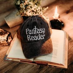 a hat that reads fantasy reader sitting on top of an open book next to a lit candle