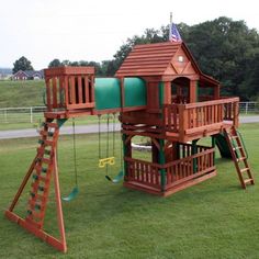 a wooden swing set with a green slide and climbing frame in the middle of grass