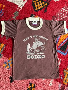 "You won't want to take off  this best-selling retro ringer! Vintage brown body/vintage cream ringer/vintage cream dillas cowboy graphic   Machine wash cold, tumble dry low inside out - 60% cotton / 40% polyester SIZE      CHEST     LENGTH FROM SHOULDER XSmall36\"       26.5\" Small38\"       27\" Medium40\"       27.5\" Large42\"       28\" XLarge44\"         28.5\"" Vintage Ringer Tshirt, Unisex Vintage T-shirt With Letter Print, Vintage Unisex T-shirt With Letter Print, Ringer Tee Vintage, Vintage Graphic Print T-shirt For Adventure, Vintage Adventure Graphic T-shirt, Vintage Short Sleeve T-shirt For Adventure, Vintage Crew Neck Tops For Adventure, Not My First Rodeo