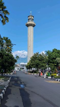 a tall tower with a clock on top in the middle of a street next to palm trees