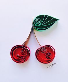 two red paper flowers sitting on top of a white table next to a green leaf