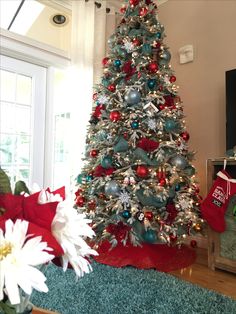 a christmas tree with red, blue and silver ornaments is in the middle of a living room