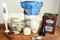 an assortment of ingredients are displayed on a wooden table next to a blender and spoon