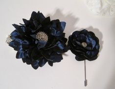 two black flowers on a white surface next to a flower headband and brooch