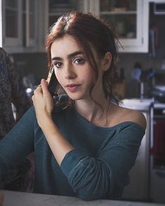 a woman is talking on her cell phone while sitting at the kitchen table with another person in the background