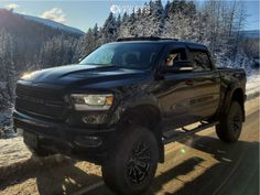 a black truck driving down a road next to snow covered mountains and trees in the background