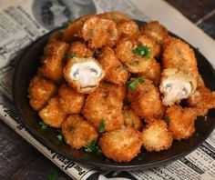 fried food in a black bowl on top of a newspaper next to utensils