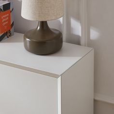 a lamp sitting on top of a white dresser next to a book and an orange sign