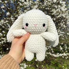 a hand holding a white crocheted stuffed animal in front of a flowering tree