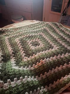 a crocheted blanket sitting on top of a bed next to a wooden dresser