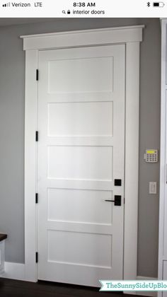 a white door in the corner of a room with gray walls and wood flooring