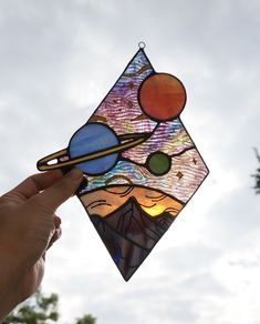 a hand holding a stained glass sun catcher in front of the sky with planets and saturn on it