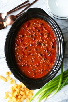 a crock pot filled with chili and beans next to some spoons on a table