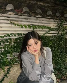 a woman sitting on the ground with her hand under her chin and looking at the camera