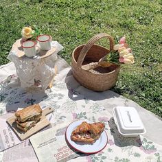 a picnic table with sandwiches and tea on it in the grass next to a basket full of flowers