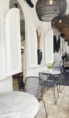 an outdoor dining area with chairs, tables and umbrellas hanging from the ceiling in front of white shuttered windows