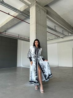 a woman is standing in an empty room with her hand on her hip and wearing a long black and white coat