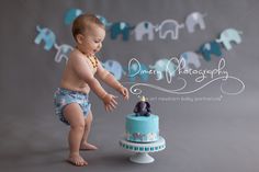 a baby in diapers reaching for a cake with an elephant decoration on the top