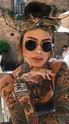 a woman with tattoos on her arms and chest, wearing sunglasses and a bandana