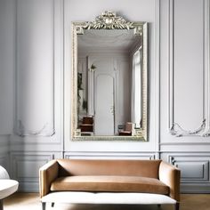 a couch sitting in front of a large mirror on the side of a white wall