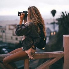 a woman sitting on top of a wooden railing taking a photo with her cell phone